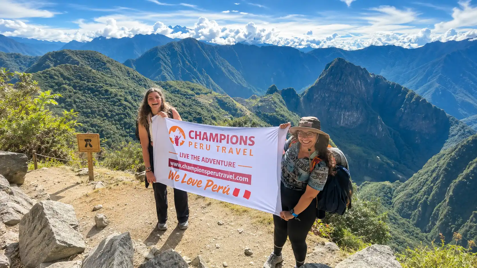 Two hikers holding a Champions Peru Travel banner with Machu Picchu and the Andes mountains in the background