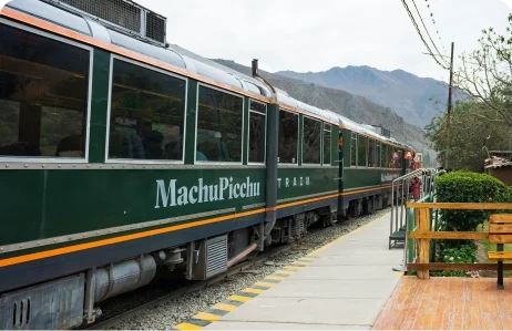 Green Machu Picchu train stopped at a railway platform surrounded by mountain scenery