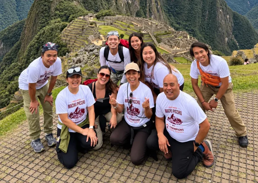 Group of travelers posing at Machu Picchu with the ancient Inca citadel and mountains in the background